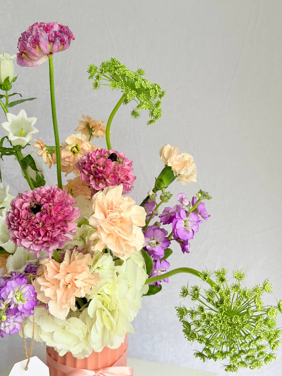 Bouquet of colorful flowers in a pink vase on a light gray background
