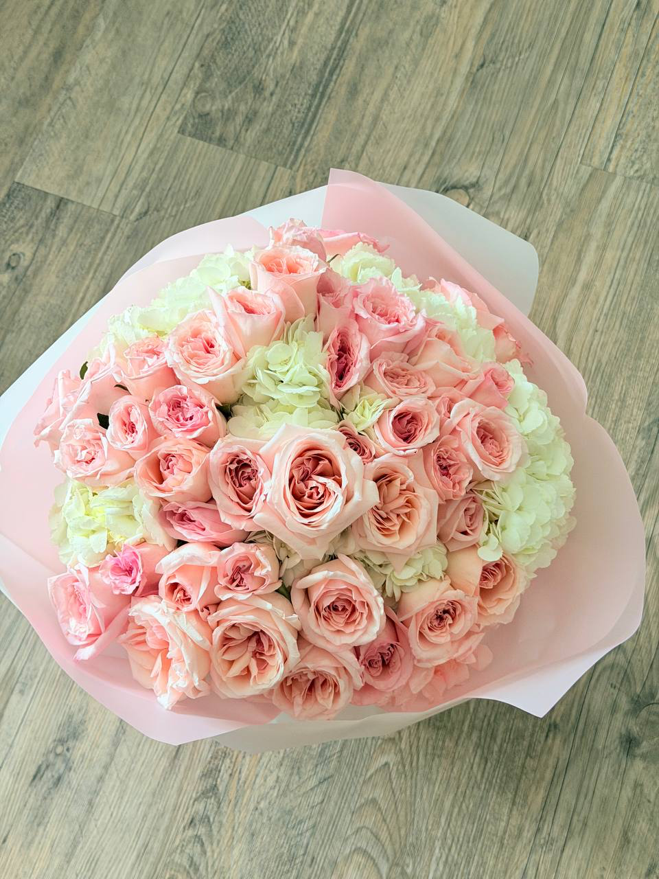 Bouquet of pink and green roses wrapped in paper on a wooden surface