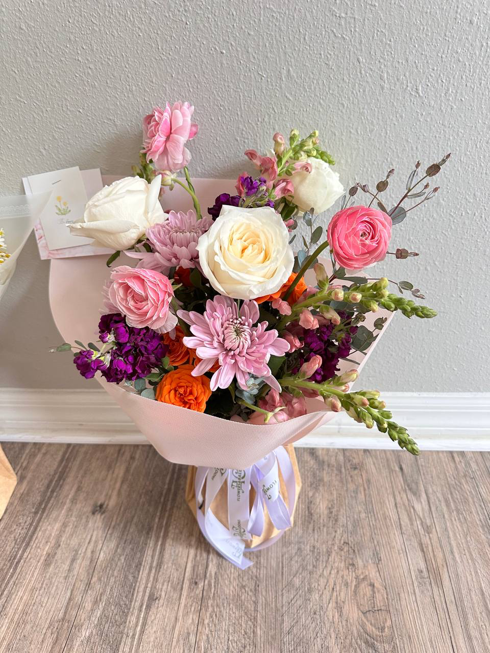 Bouquet of flowers in a pink holder on a wooden floor with a neutral wall background