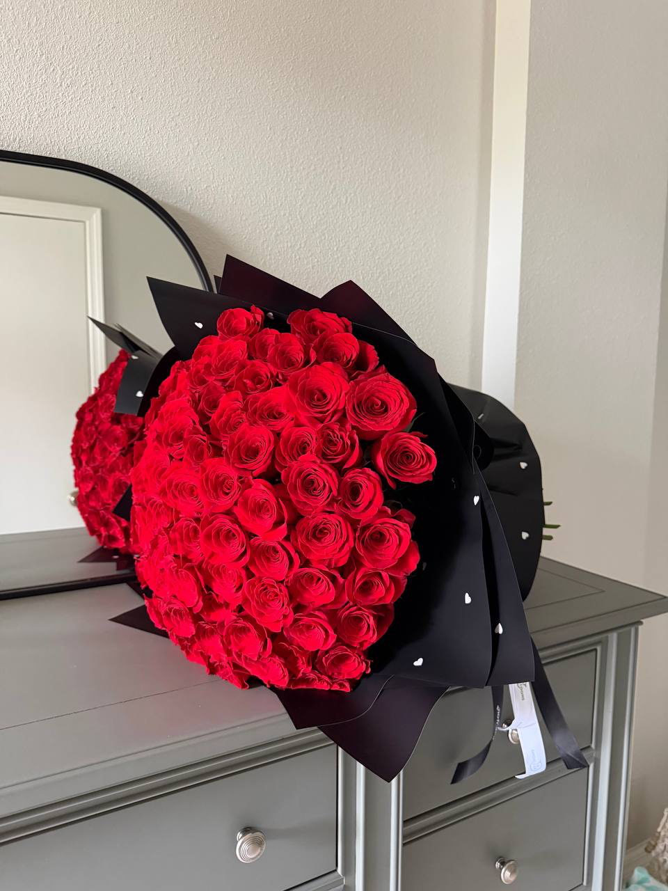 Bouquet of red roses wrapped in black paper on a dresser.