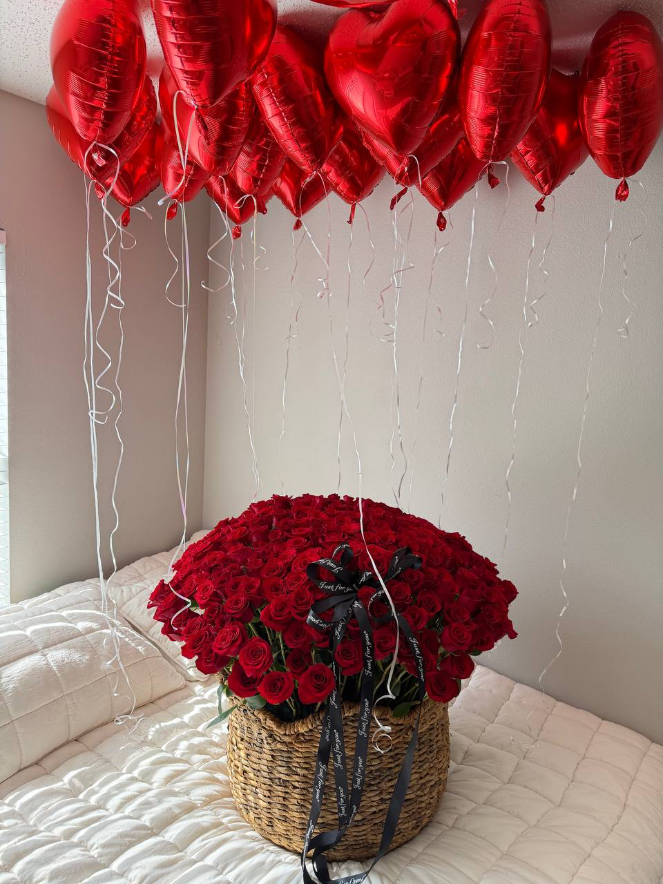 Basket of red roses on a bed with heart-shaped red balloons above