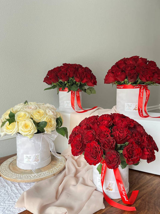 Three bouquets of red roses with white ribbons on a wooden table against a light gray wall.