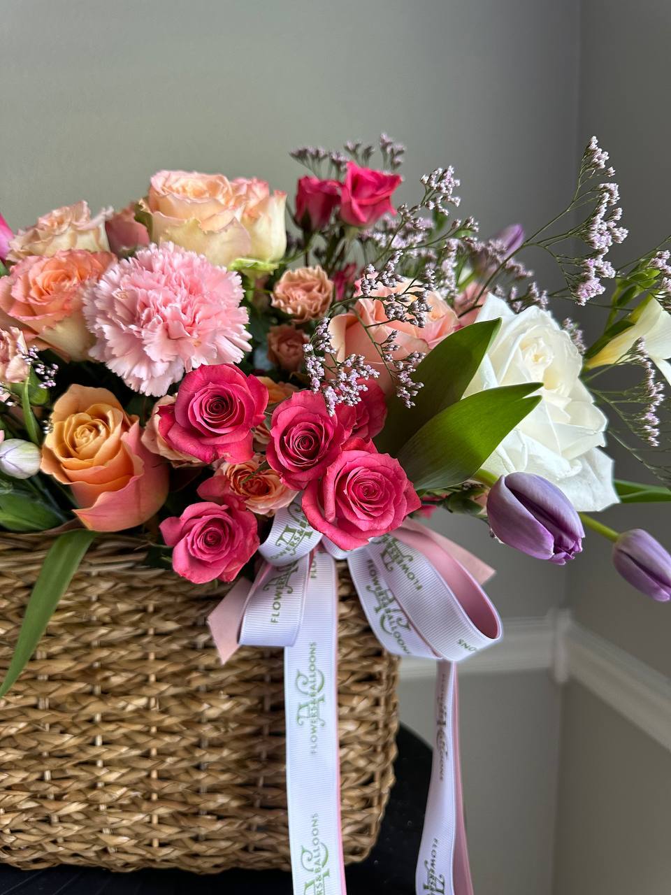 Bouquet of flowers in a woven basket with a ribbon against a neutral background