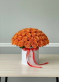 Bouquet of orange roses in a white box with a red ribbon on a light gray background