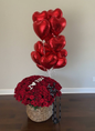 Basket of red roses with 'I love you' heart-shaped balloon and additional red heart balloons on a plain background.