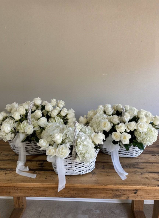 Three white flower baskets on a wooden table against a plain wall.