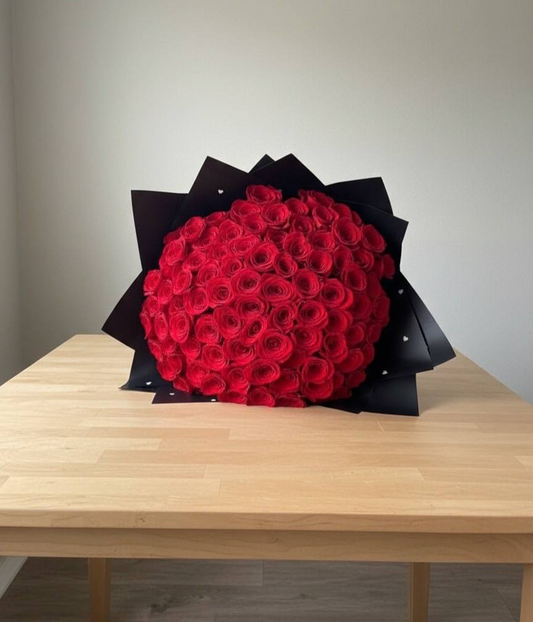 Bouquet of red roses wrapped in black paper on a wooden table with a plain background
